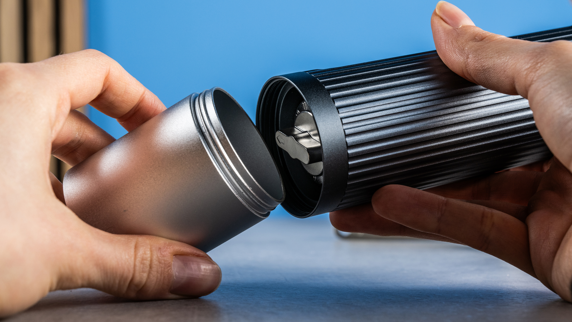 מטחנת הקפה הידנית של Aeropress בצבעי אפור וכסף על רקע הכחול של המדריך