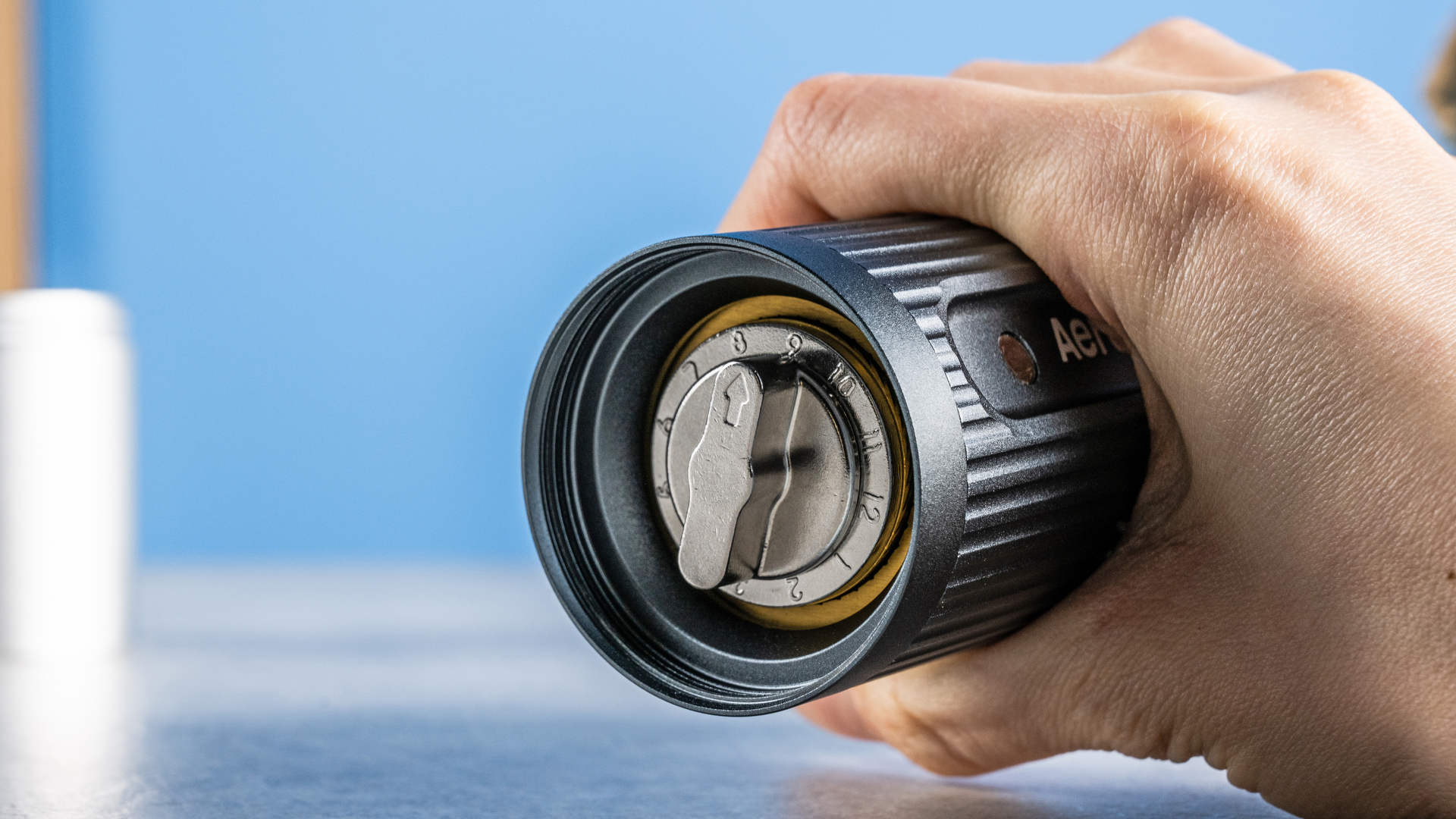 מטחנת הקפה הידנית של Aeropress בצבעי אפור וכסף על רקע הכחול של המדריך