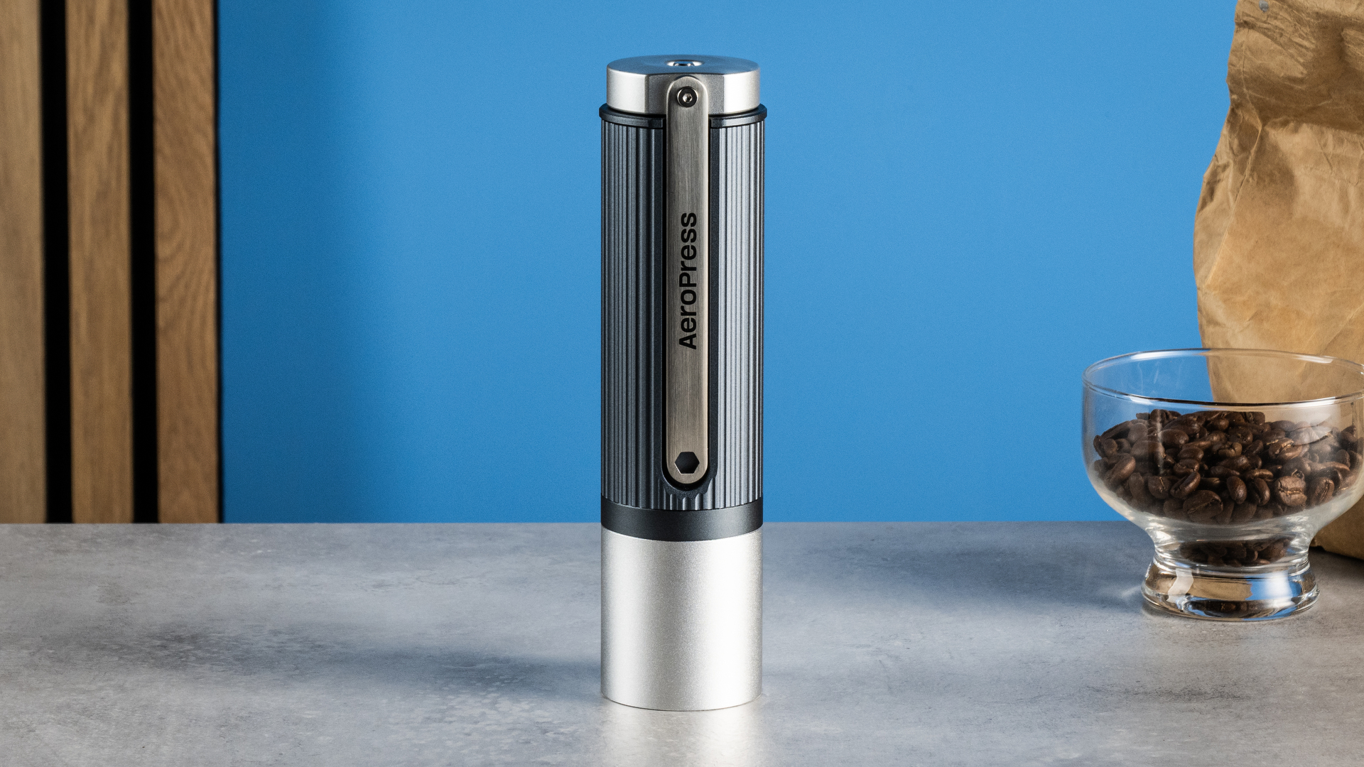 מטחנת הקפה הידנית של Aeropress בצבעי אפור וכסף על רקע הכחול של המדריך