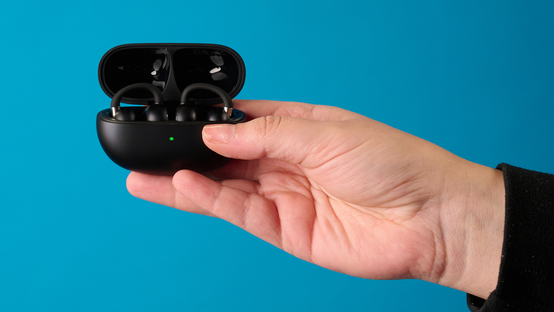האן מחזיק את ה-EarFun Clip 2 בשחור מצולם מול רקע כחול