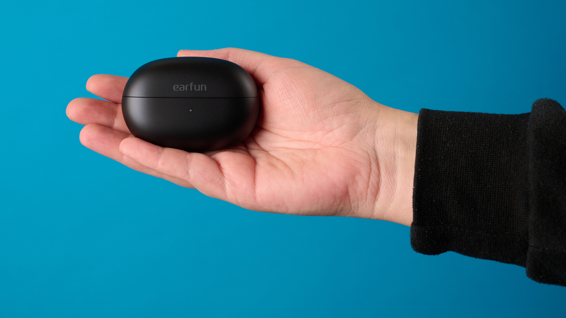 יד מחזיקה את ה-EarFun Clip 2 בשחור מצולמת מול רקע כחול