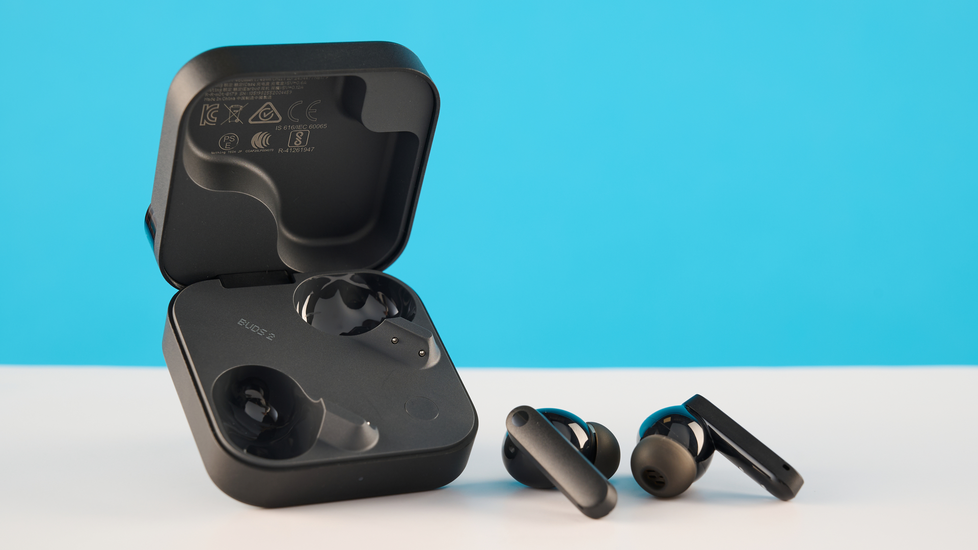 CMF Buds 2 בצילומי אפור כהה על שולחן אפור מול רקע כחול