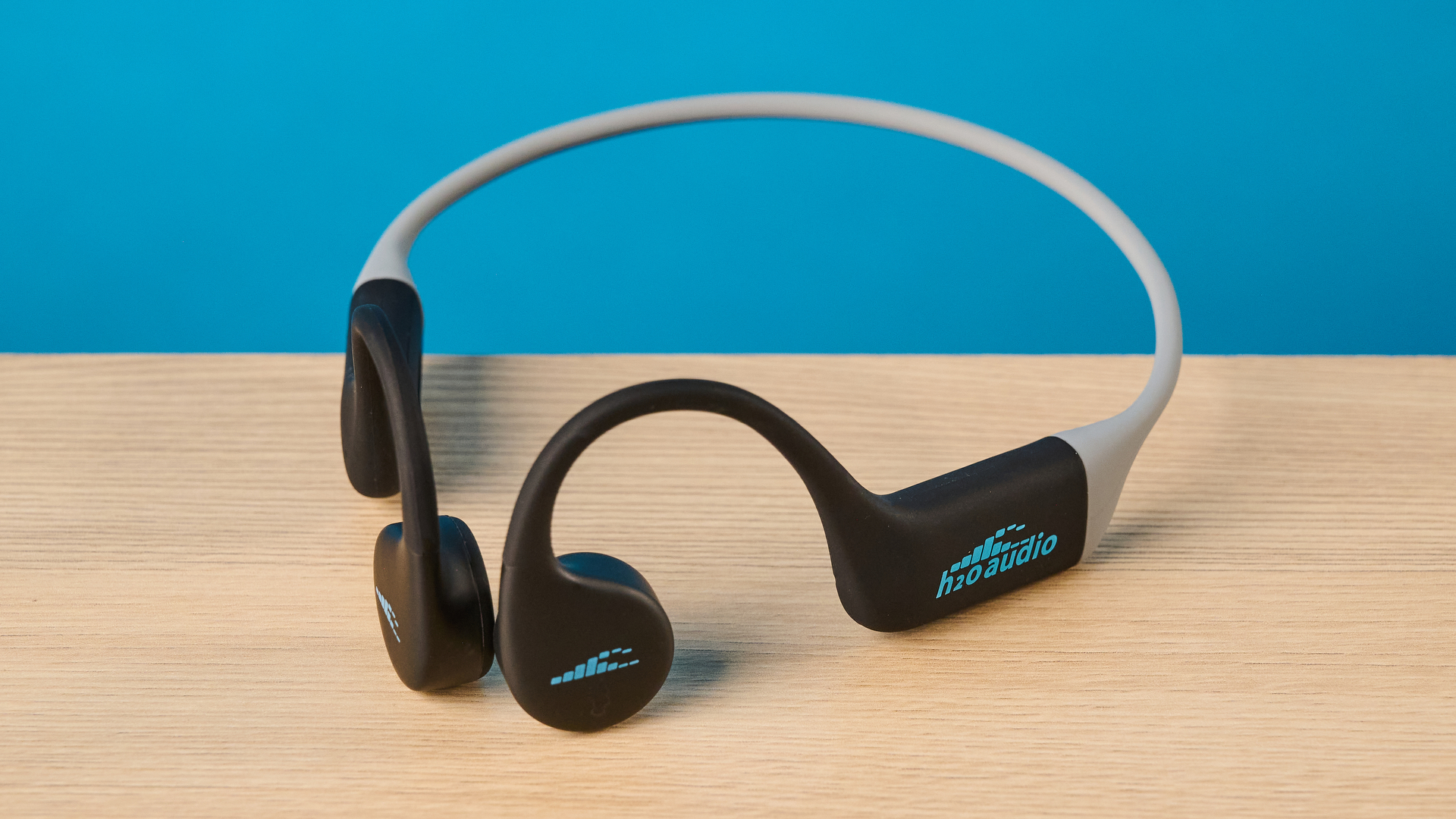 אוזניות ה-h2o audio tri run bone conduction שצולמו על רקע כחול של Tom's guide