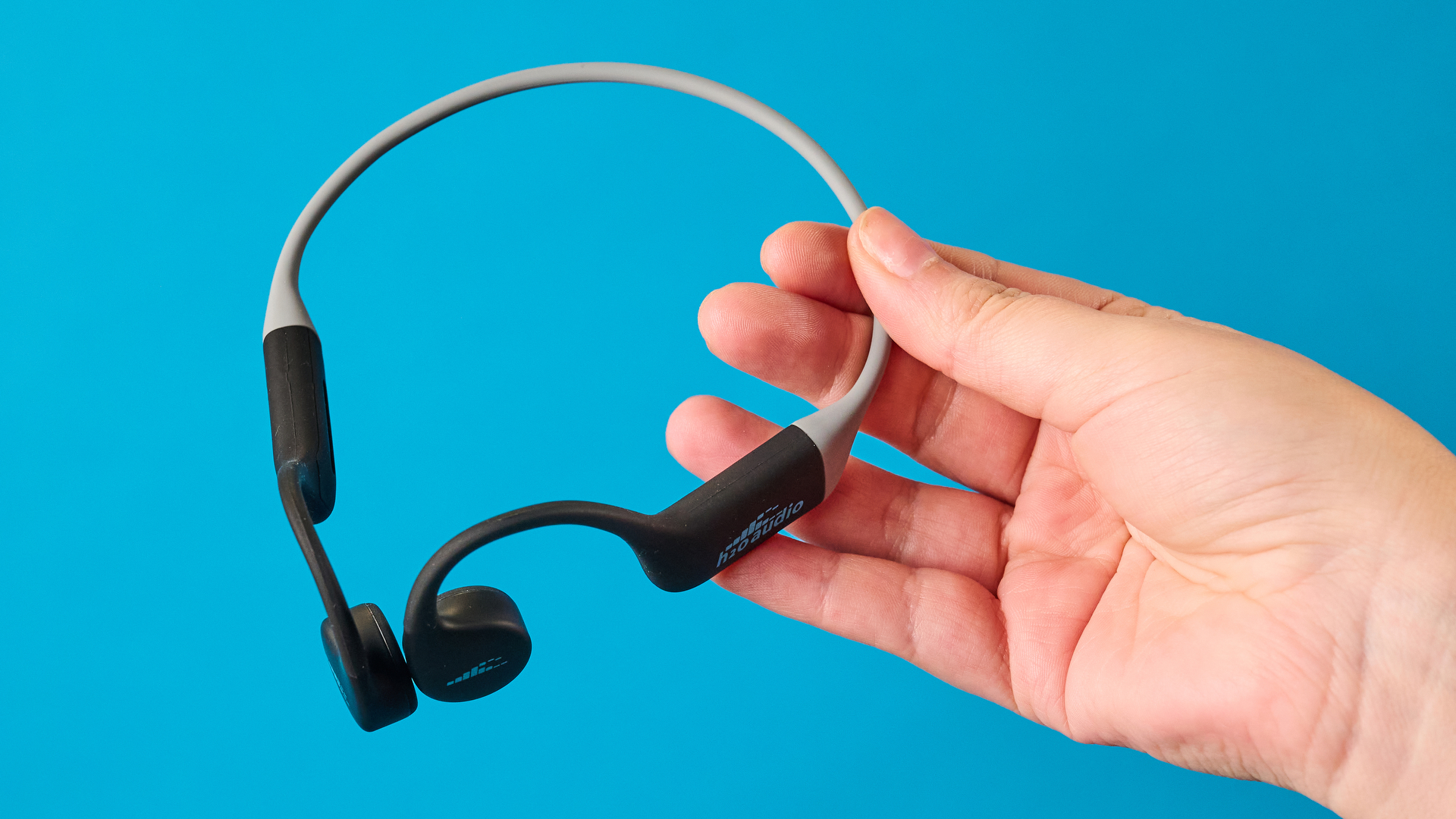 אוזניות ה-h2o audio tri run bone conduction שצולמו על רקע כחול של Tom's guide