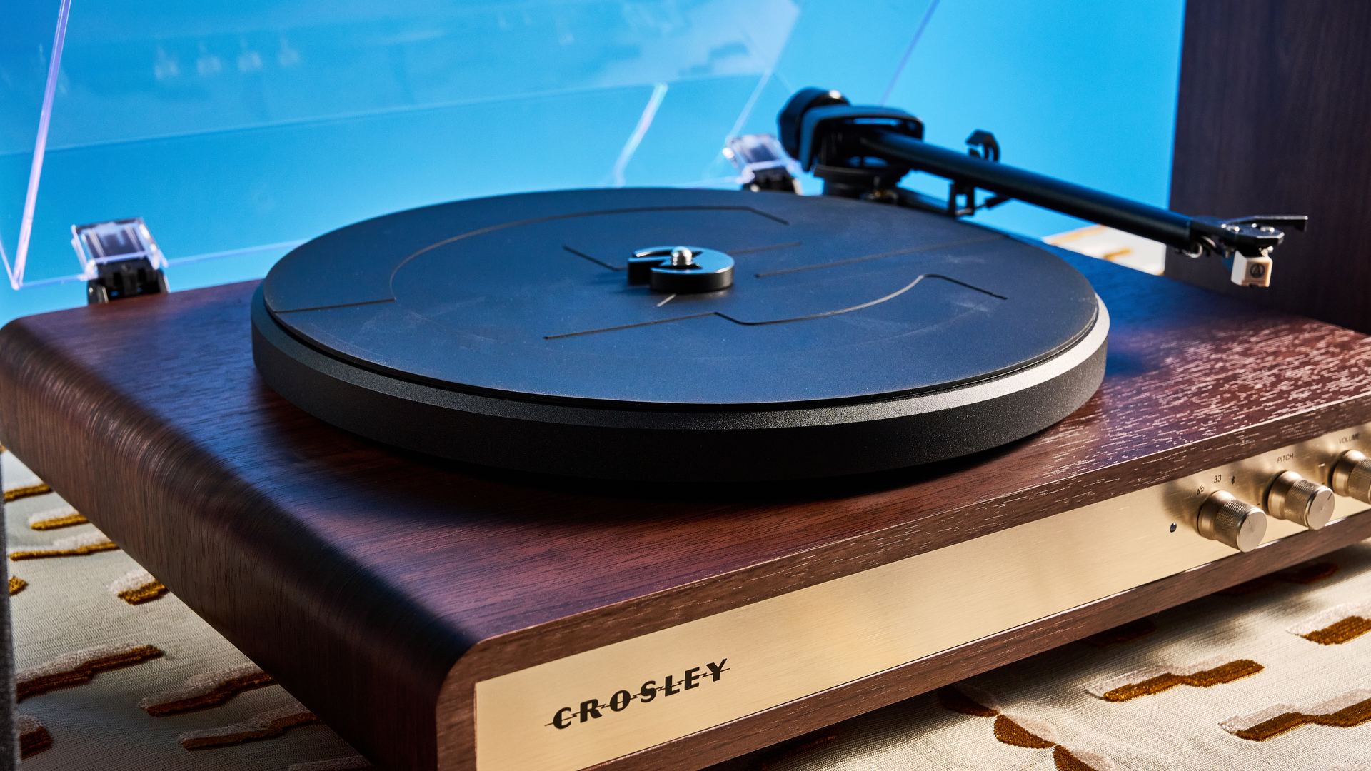 פטיפון ורמקולים מדף של Crosley C65 מצולמים מול רקע כחול על שולחן חום.