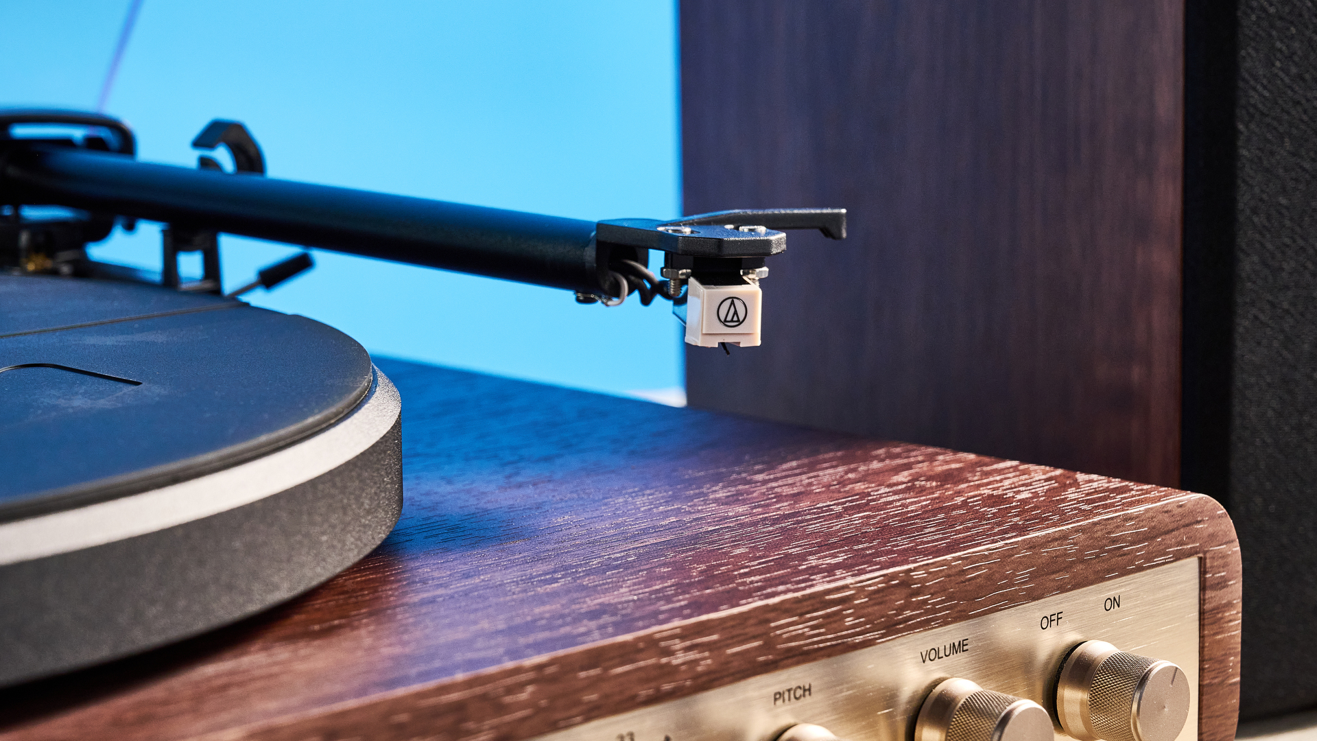פטיפון ורמקולים מדף של Crosley C65 מצולמים מול רקע כחול על שולחן חום.