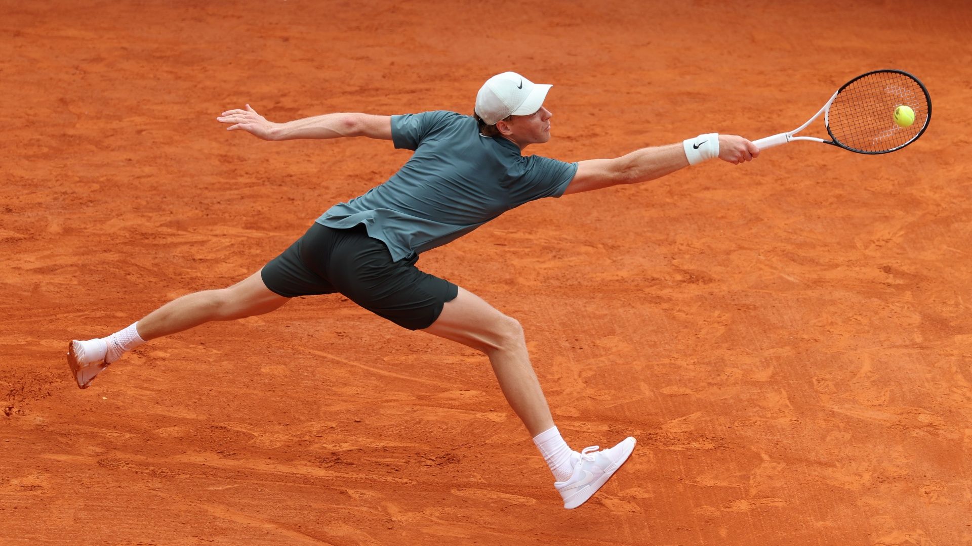 Jannik Sinner wearing white cap and green top stretches for the ball ahead of the 2026 French Open Roland Garros tennis