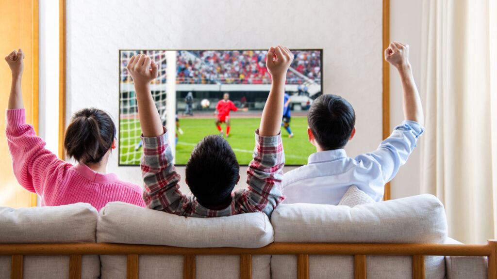 Family watching television and cheering soccer game on TV together in their living room.
