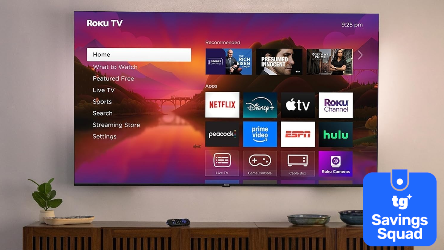טלוויזיית Roku Plus מסדרת 4K תלויה על הקיר המציגה את מסך הבית של Roku מעל קרדנזה בסלון מודרני. בפינה התחתונה יש תג סופר-מוטל עליו כתוב: "TG Savings Squad".