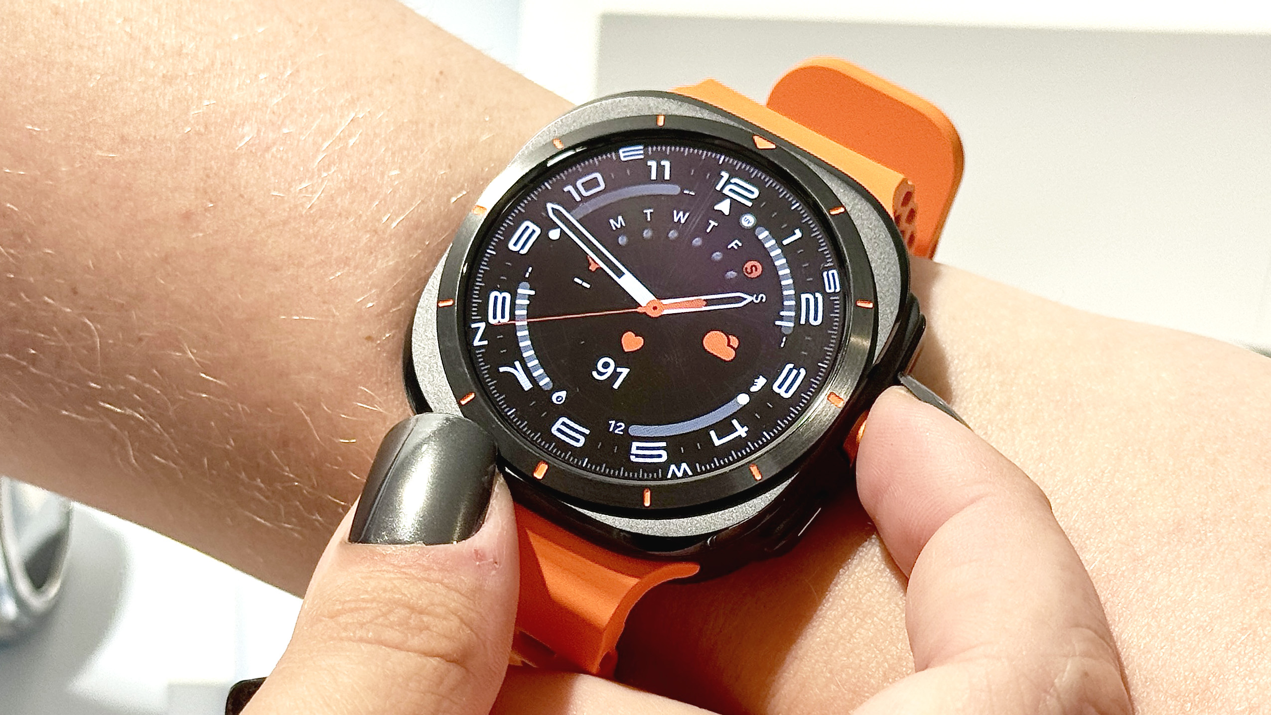 Samsung Galaxy Watch Ultra על רצועת גומי כתומה הנלבשת על פרק כף היד של משתמש