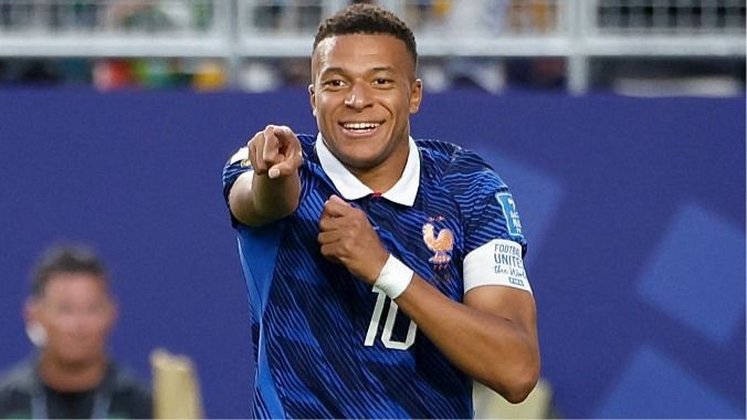 A smiling Kylian Mbappe, wearing blue, points to a team-mate during France's World Cup 2026 campaign.