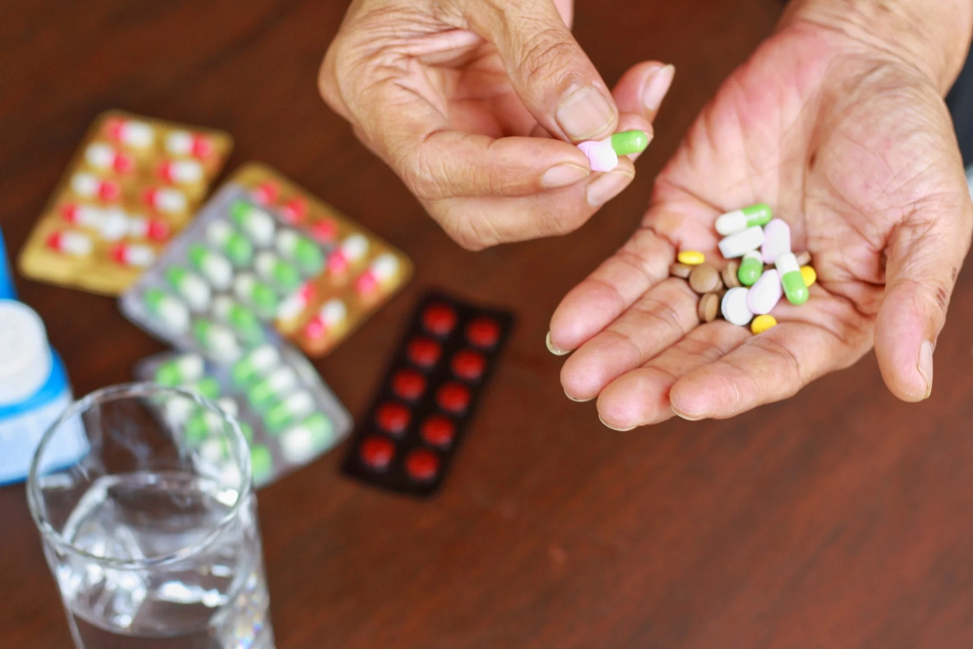 Elderly man hands holding many pills(tablet and capsule). Packets of mediation and glass of water