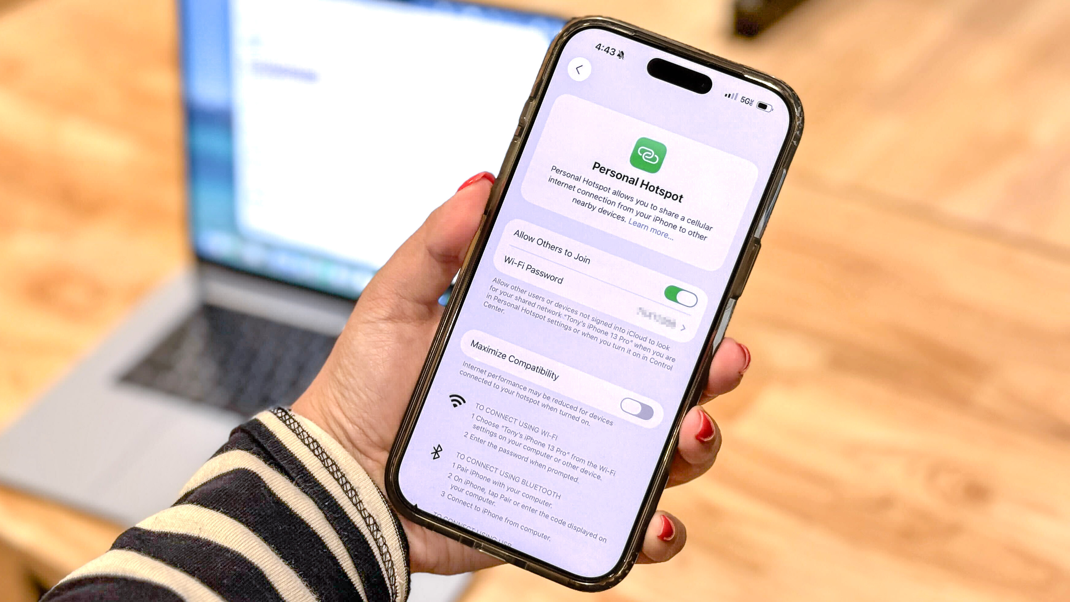 אדם מחזיק אייפון מול MacBook שמציג את iOS' תכונת נקודה חמה אישית