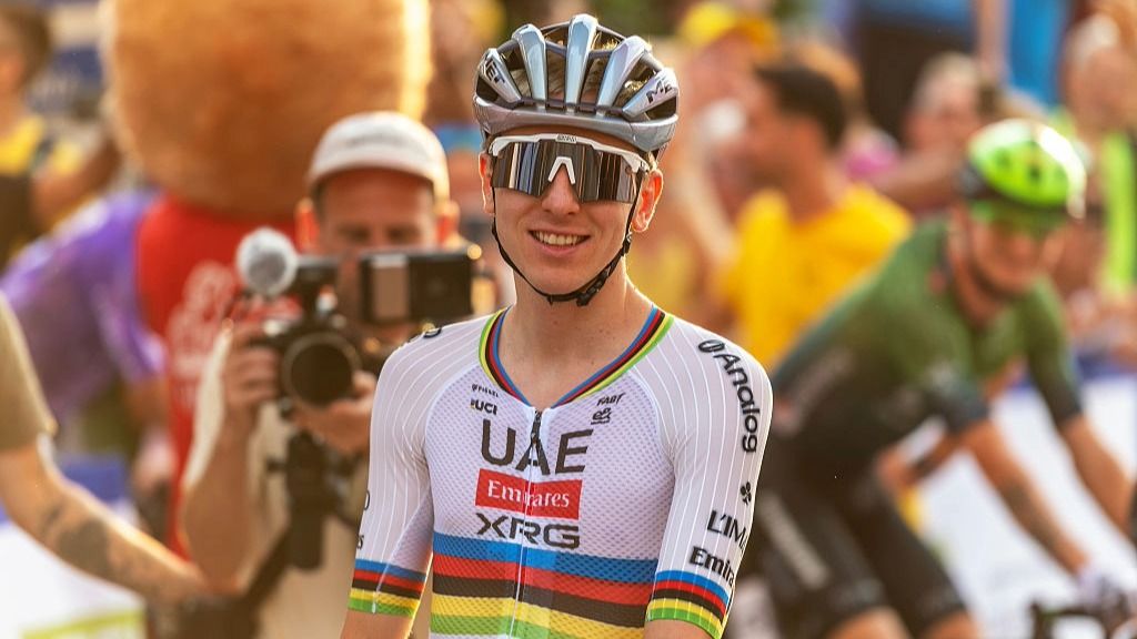 Tadej Pogacar, wearing a cycling helmet and rainbow colors of the world champion, smiles at the end of a cycling race.
