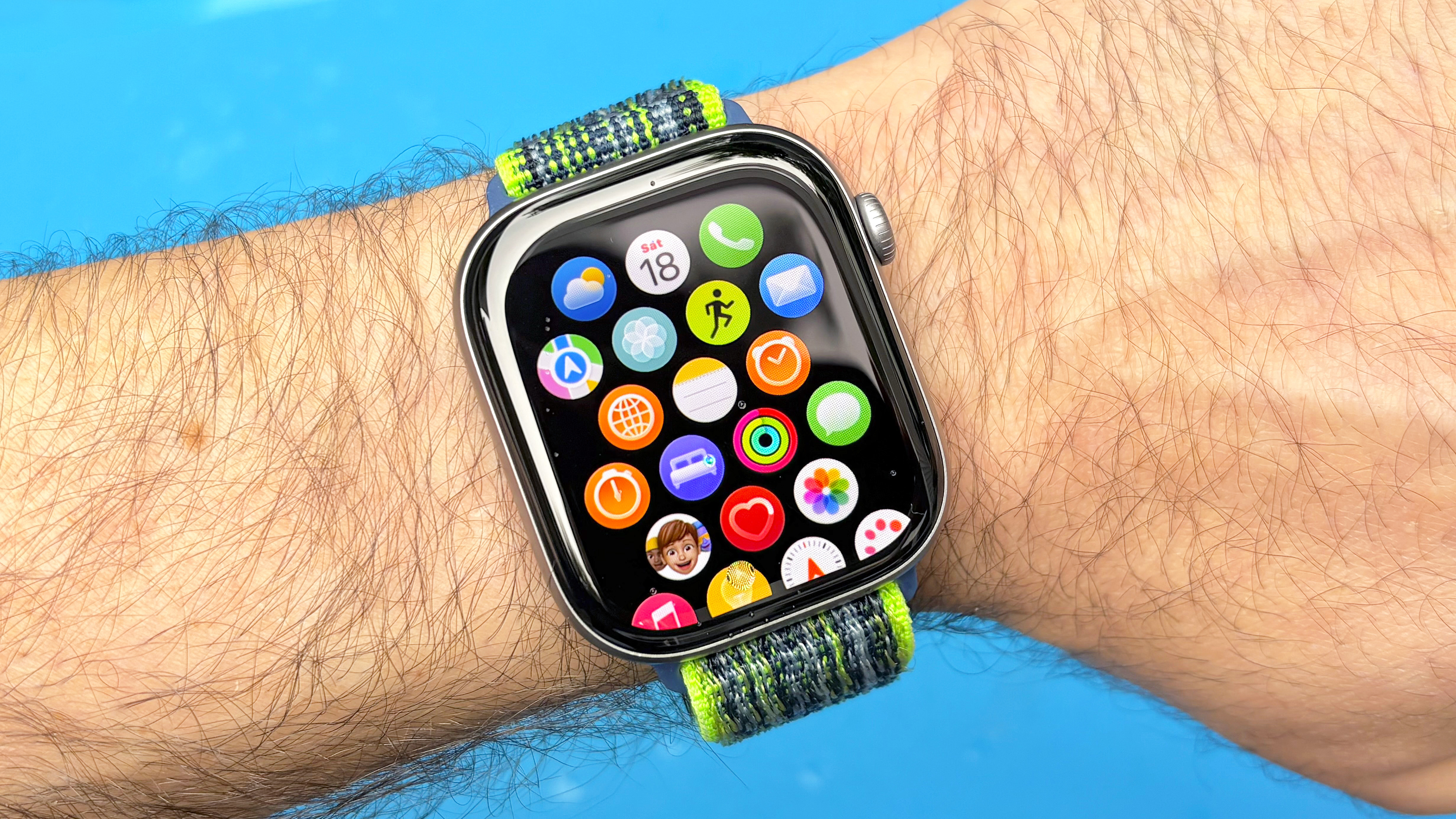 תקריב של Apple Watch 11 על פרק כף היד של משתמש על רקע כחול עם רשת סמל האפליקציה מוצגת על המסך