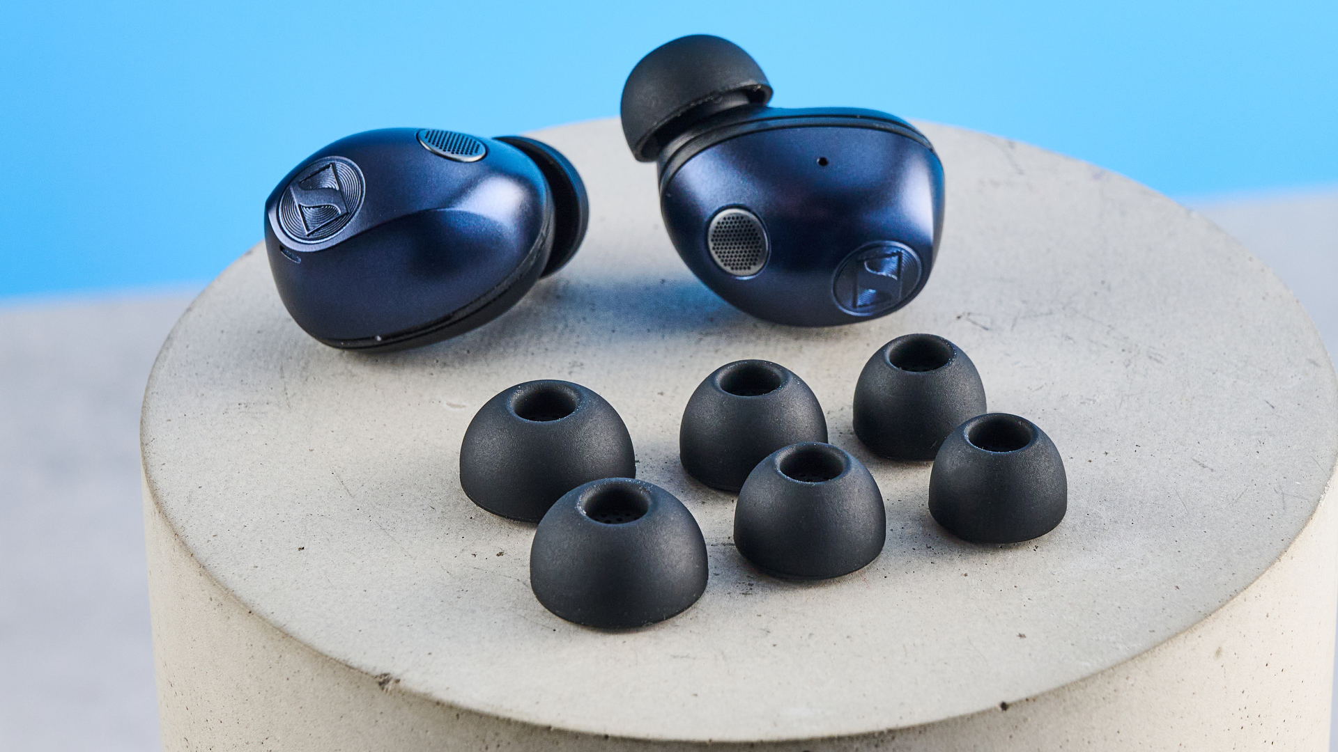 ה- Sennheiser momentum 5 אוזניות אלחוטיות אמיתיות בצבע כחול מצולמים עם רקע המדריך הכחול