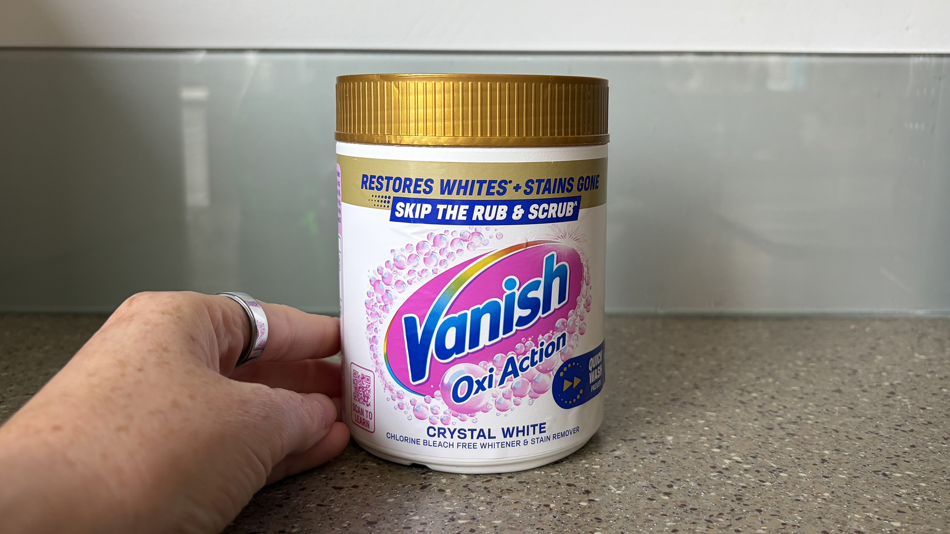 תקריב של יד ליד אמבט של Vanish OxiAction Oxygen Bleach על דלפק במטבח