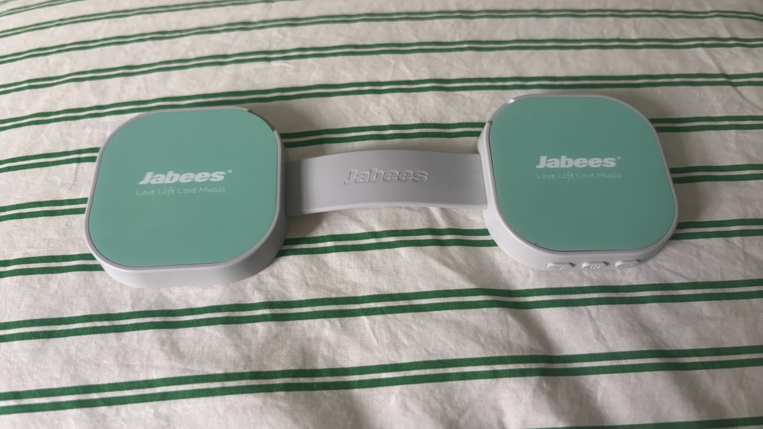 רמקול הכרית של Jabees PEACE Duo על כיסוי שמיכת פוך בפס טנדם.