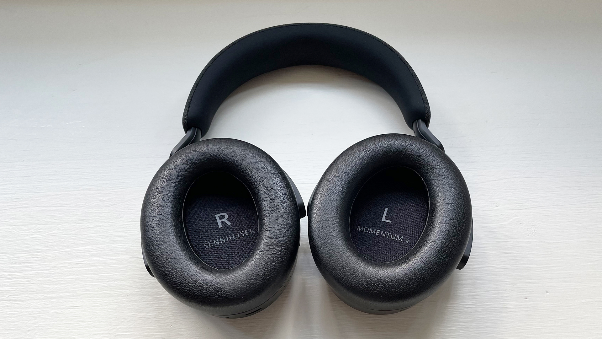 Sennheiser Momentum 4 Wireless על משטח עץ צבוע המציג בתוך כיסויי אוזניים