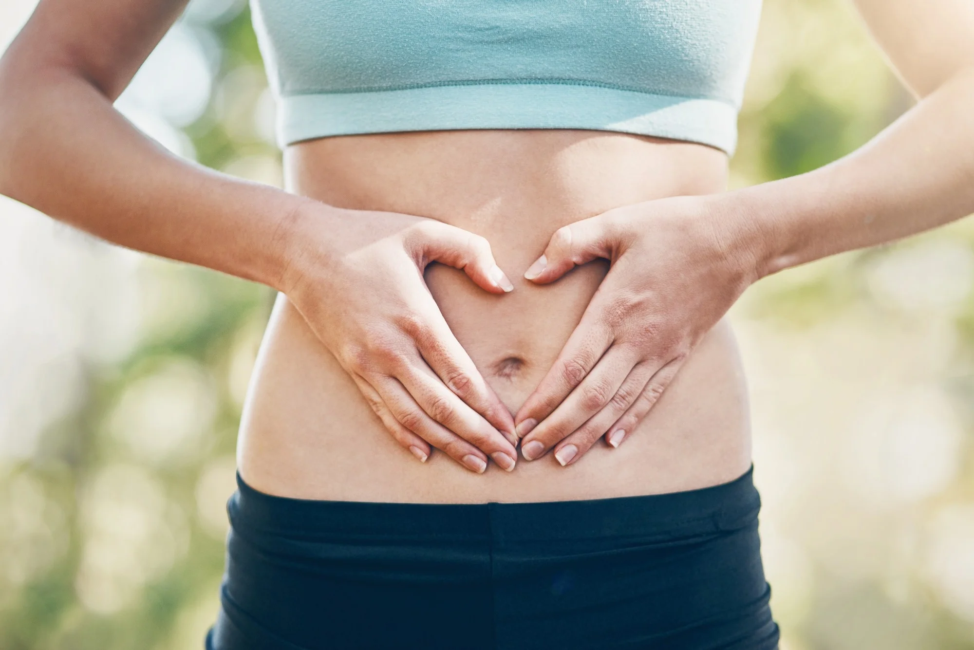 Abdomen of woman in sports gear. Hands are across stomach in the shape of a heart for gut health