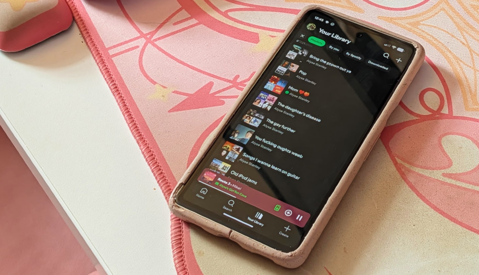 תמונה של Pixel 7a עם אפליקציית Spotify מונחת על מחצלת שולחן ורודה.
