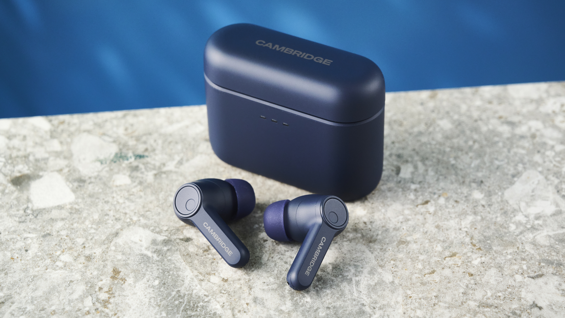 האוזניות של cambridge audio a100 se על רקע מדריך כחול עם שולחן בצבע אבן מתחת