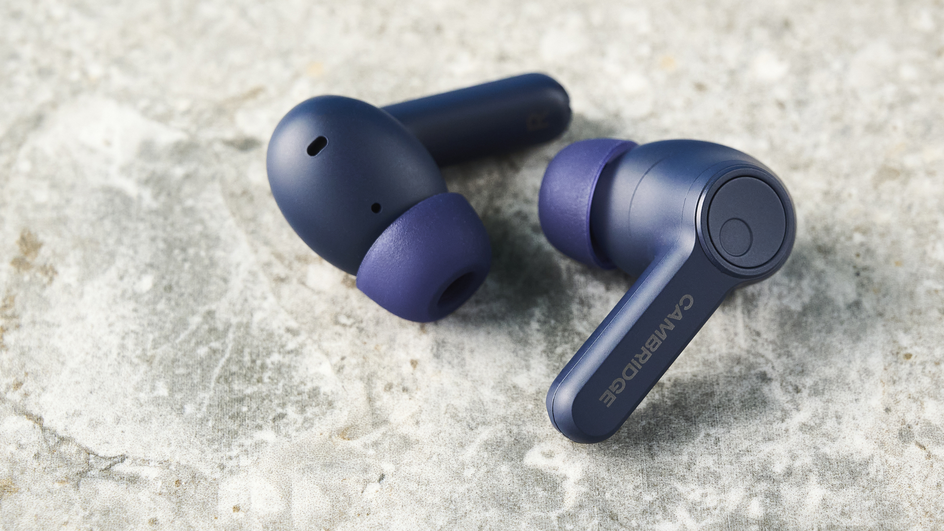 האוזניות של cambridge audio a100 se על רקע מדריך כחול עם שולחן בצבע אבן מתחת