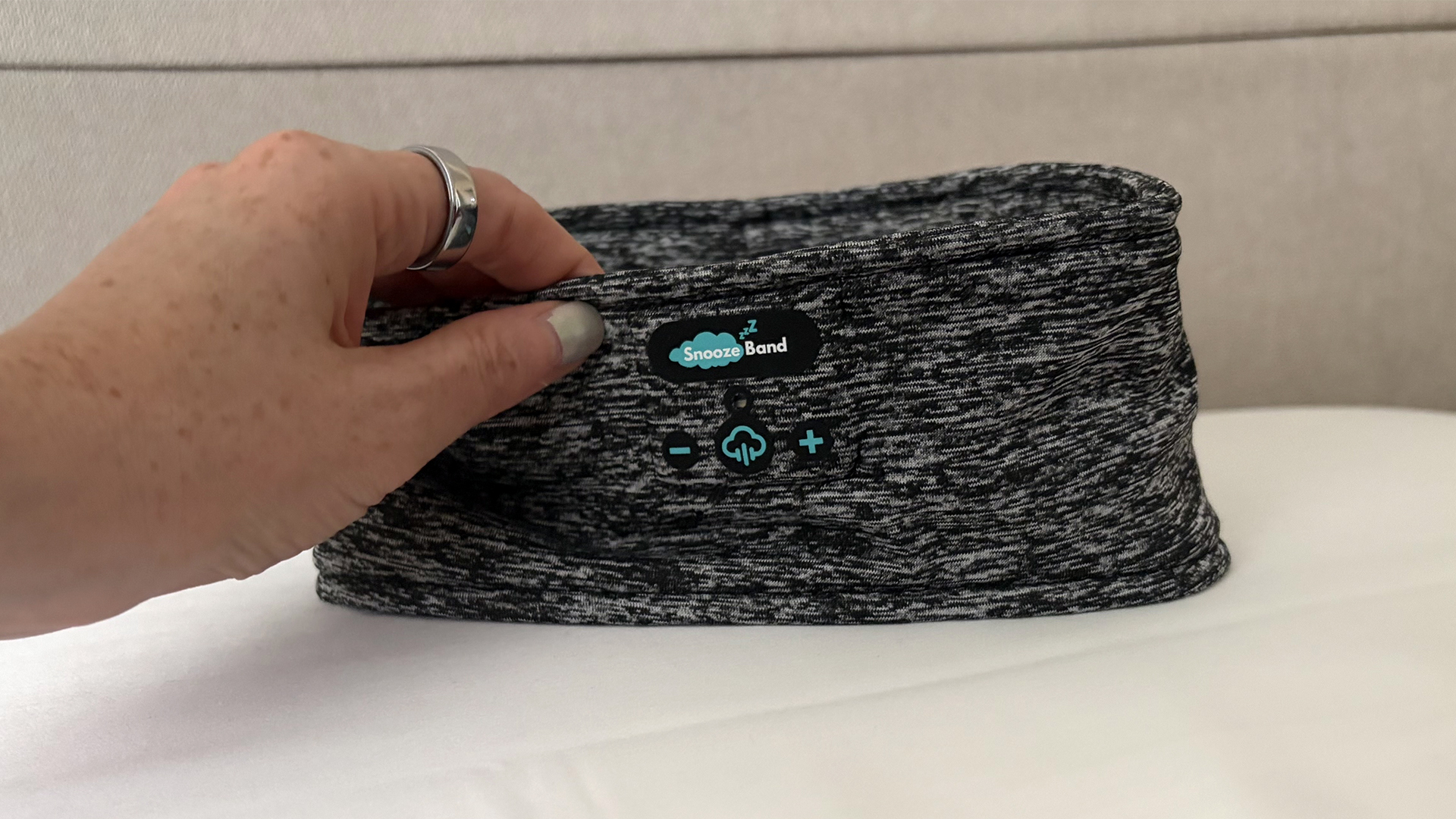יד מושטת לגעת באוזניות SnoozeBand Original Sleep, מתאזנת על כרית בחדר השינה של המבקר שלנו