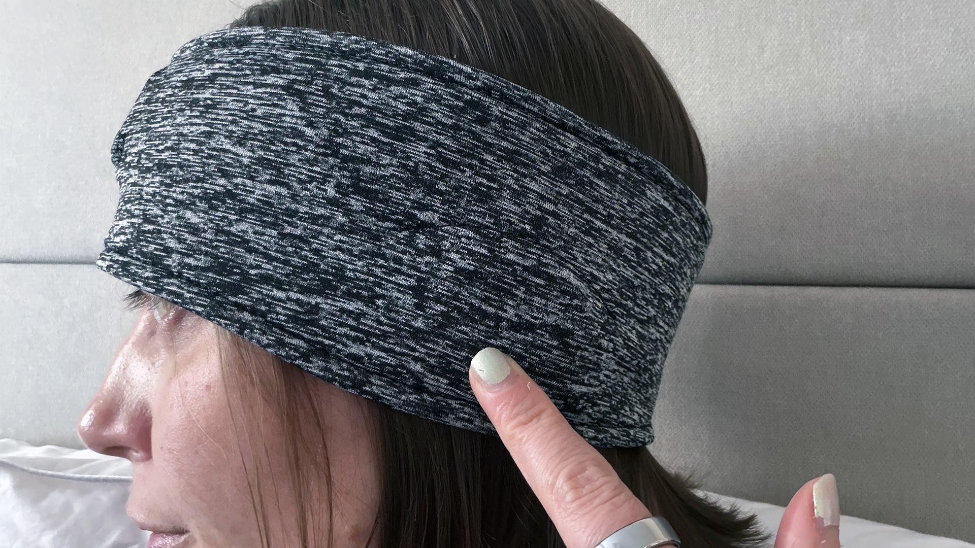 תקריב של המבקרת שלנו לובשת את ה-Snoozeband כשראשה מופנה הצידה. היא מצביעה על המקום שבו יושב הדובר