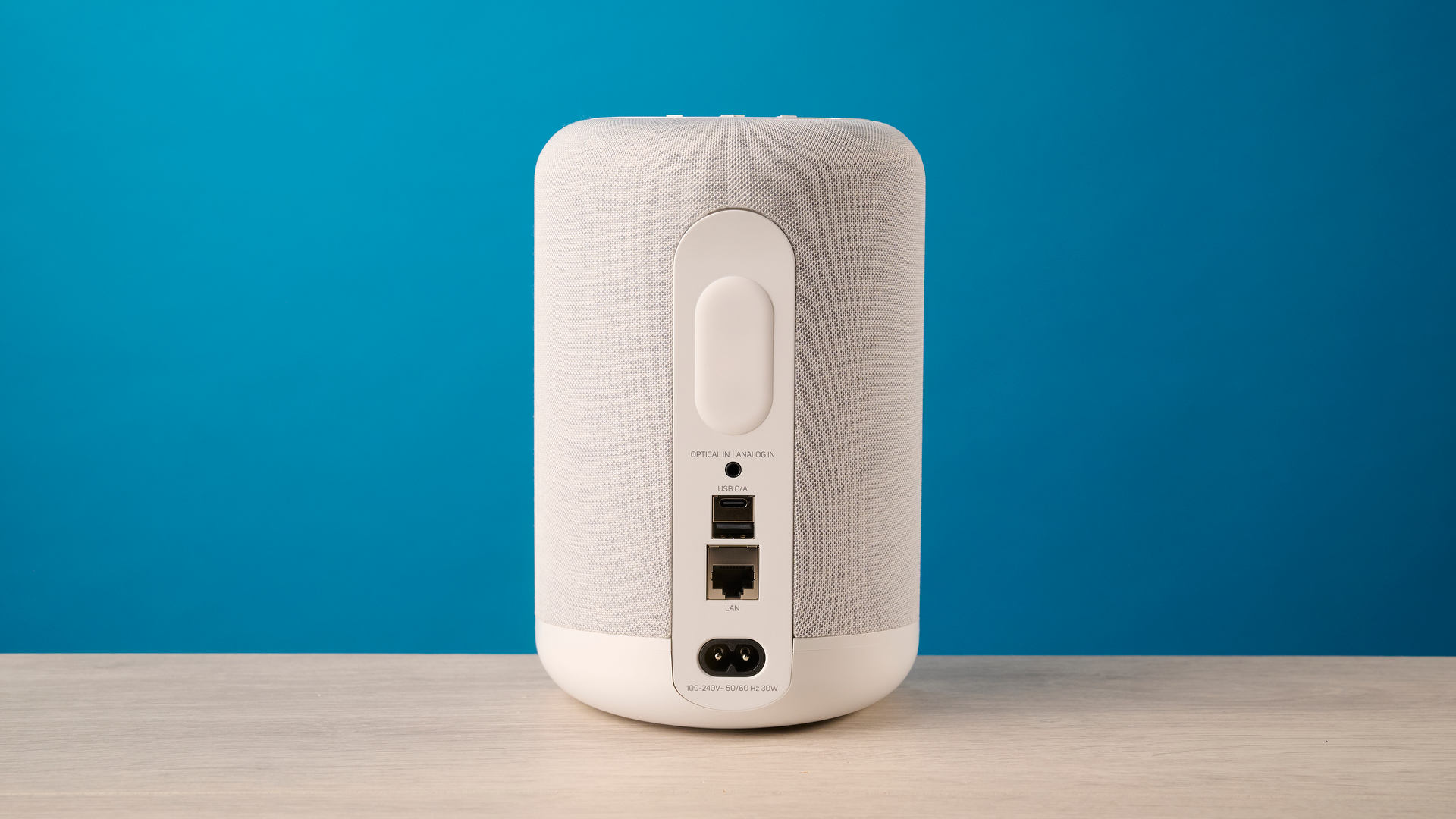 רמקול ה- bluesound pulse flex wi-fi באפור בהיר צולם על רקע המדריך הכחול של Tom's