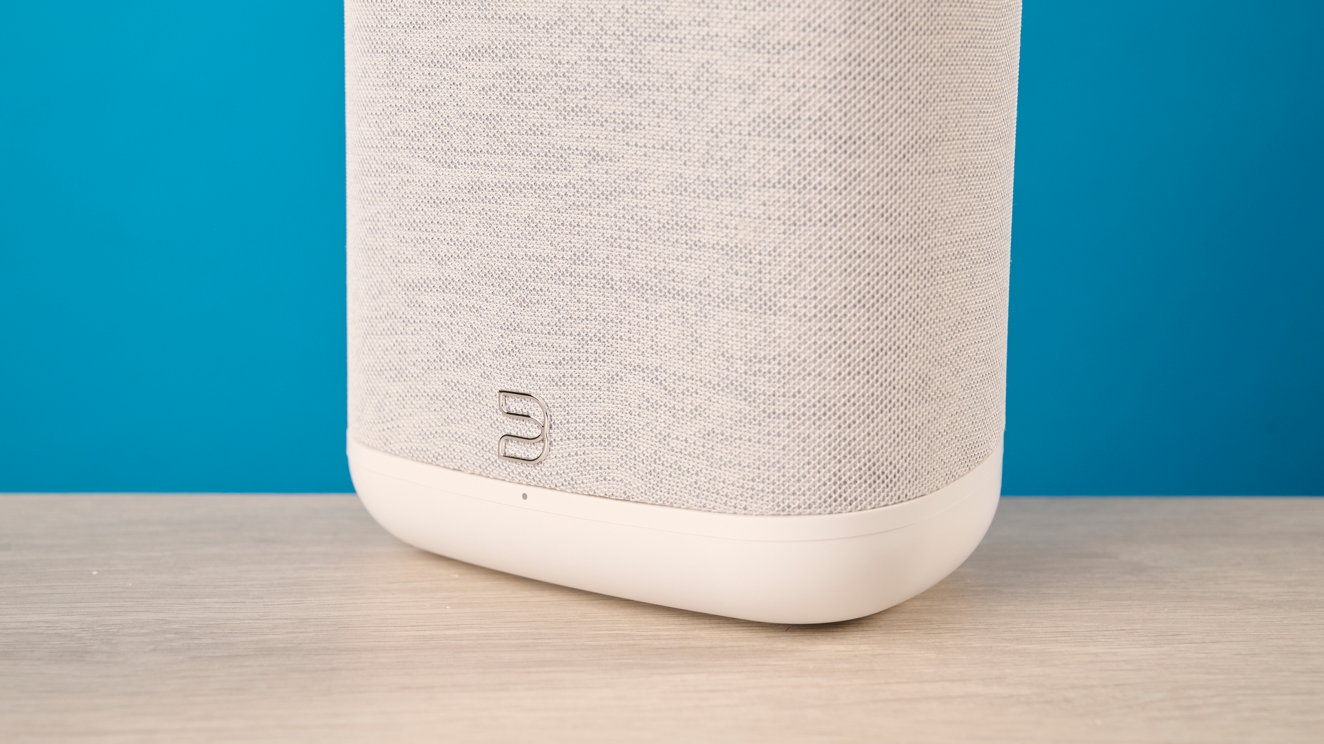 רמקול ה- bluesound pulse flex wi-fi באפור בהיר צולם על רקע המדריך הכחול של Tom's
