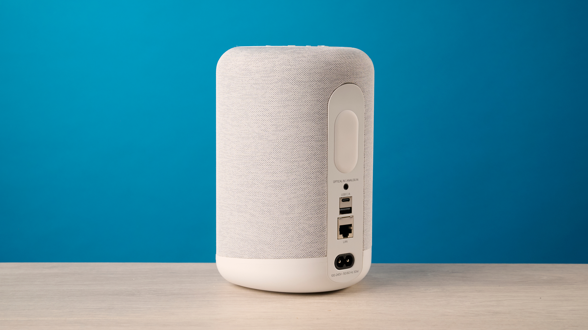 רמקול ה- bluesound pulse flex wi-fi באפור בהיר צולם על רקע המדריך הכחול של Tom's