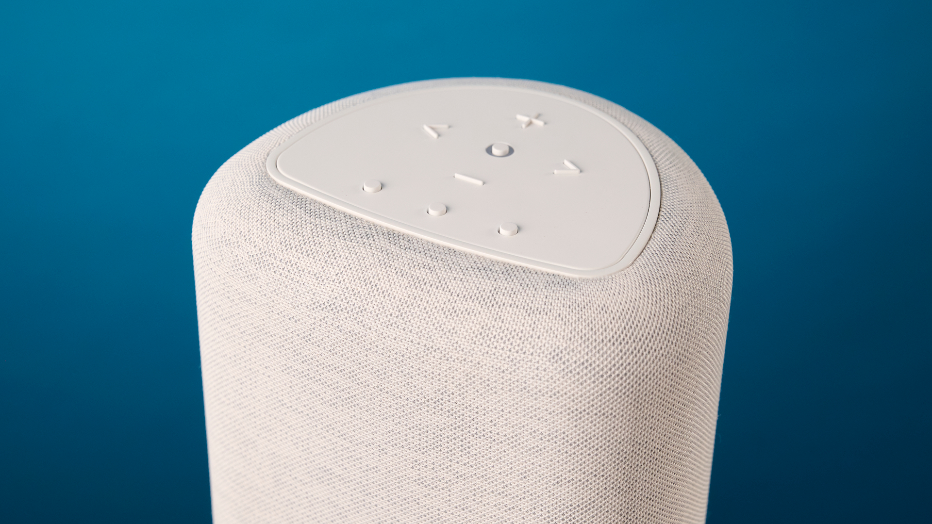 רמקול ה- bluesound pulse flex wi-fi באפור בהיר צולם על רקע המדריך הכחול של Tom's