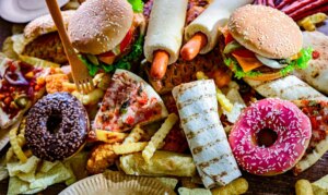 Assortment of ultraprocessed foods, including burgers, hot dogs, pizza, fries, and colorful doughnuts.