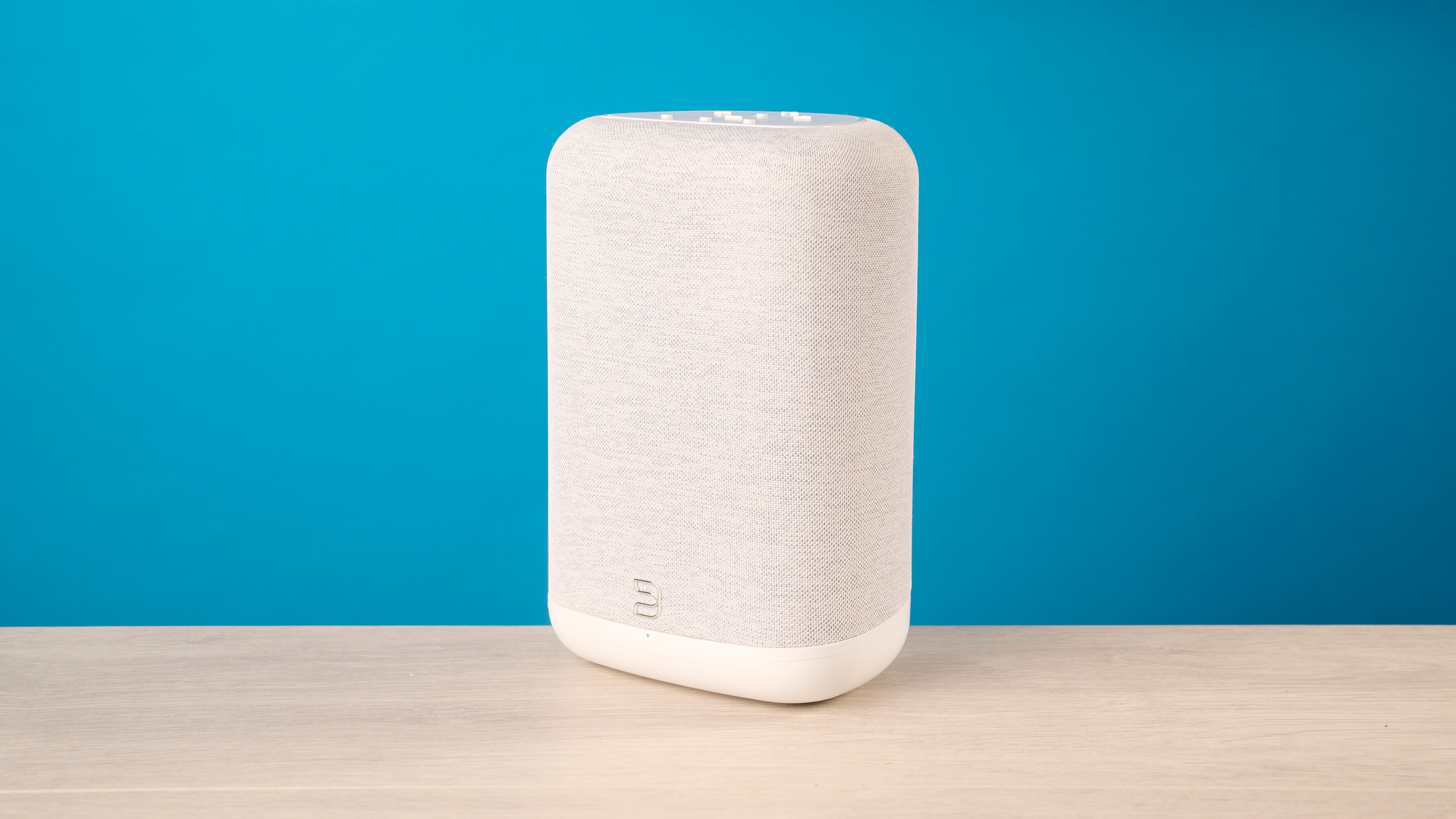 רמקול ה- bluesound pulse flex wi-fi באפור בהיר צולם על רקע המדריך הכחול של Tom's