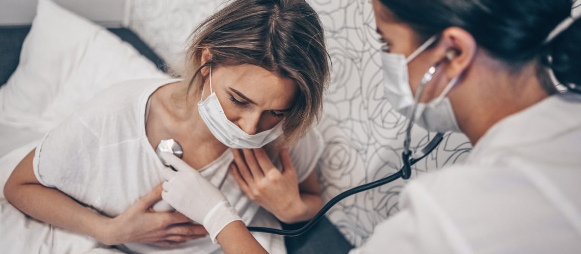 Doctor nurse in protective face mask listening to breath with a stethoscope suspecting Coronavirus (COVID-19)