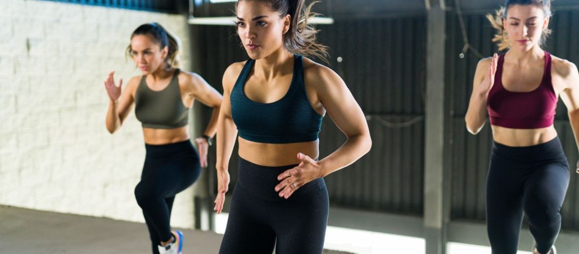 Three women exercising together at the gym with a HIIT routine running on the spot