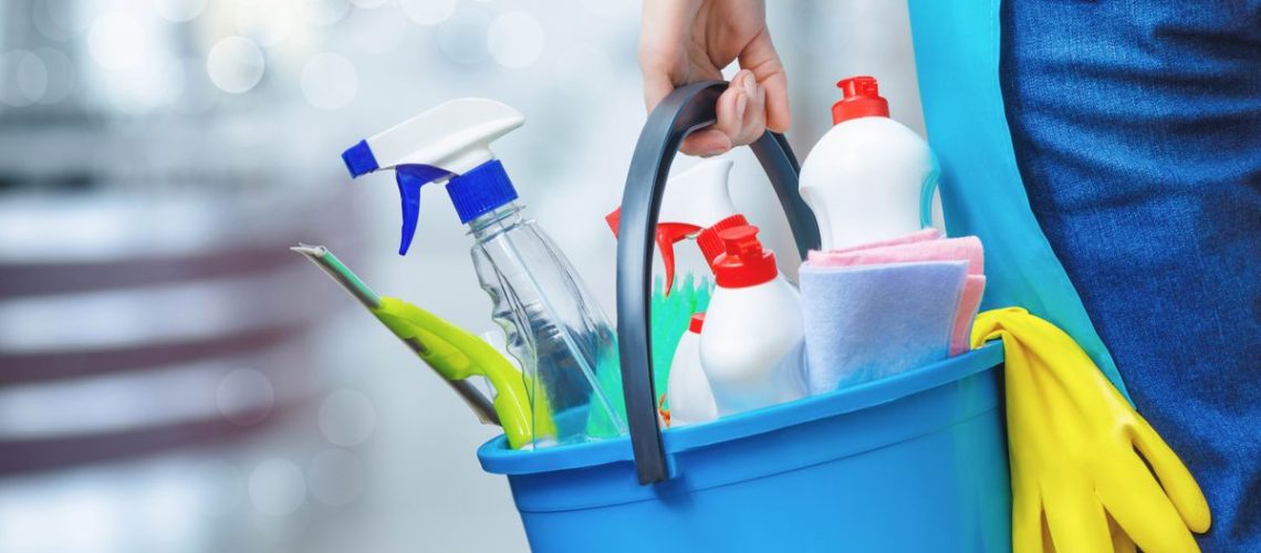 Cleaning equipment being carried in a bucket including a squeegee, cloths and spray bottles