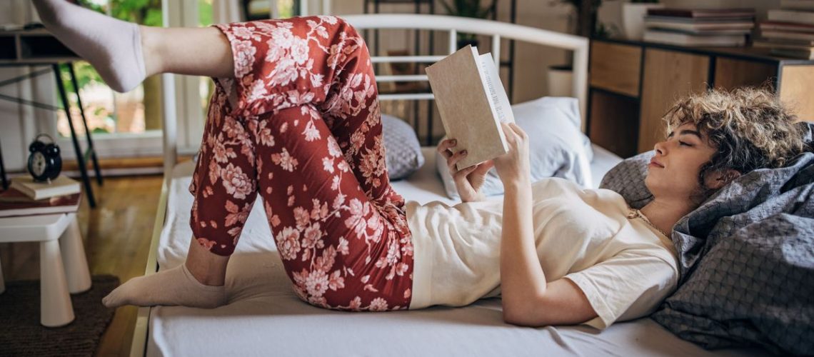 A woman with dark curly hair wears floral pyjamas while reading in bed as part of her nighttime routine