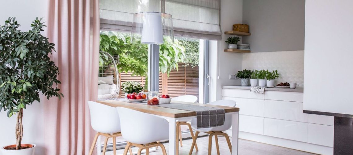 White kitchen with white table and chairs and pale pink curtains