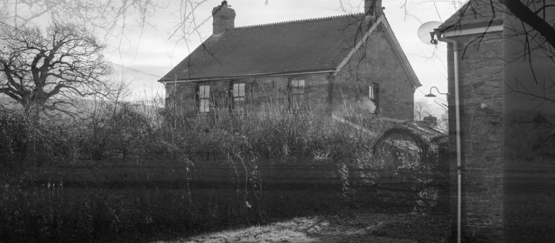 A black and white double exposure of a farmhouse with the silhouette of trees around the edges of the frame
