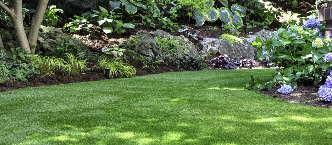 An artificial lawn in a back yard with flowerbeds and plants