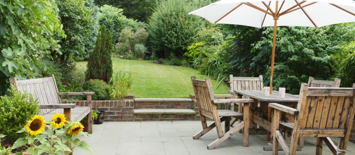 Patio in foreground of garden with bench and table and chairs to the side