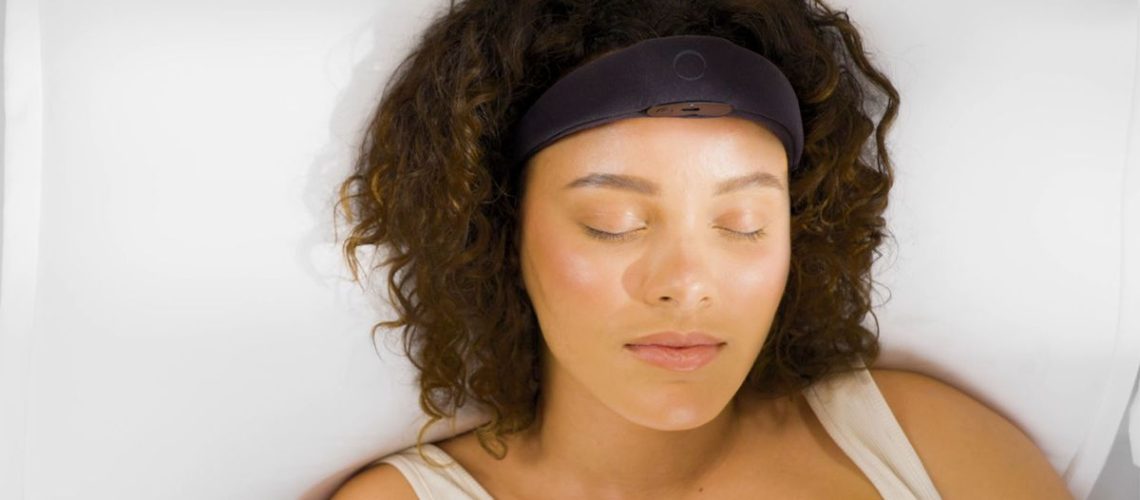 A woman lies in bed wearing the Elemind neurotech headband, she