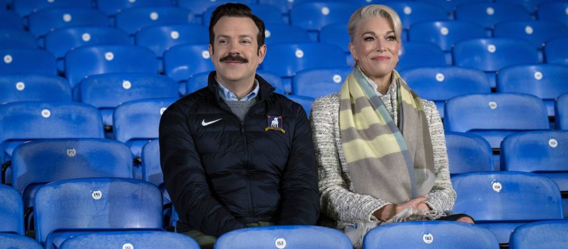 Ted Lasso (Jason Sudeikis) and Rebecca Welton (Hannah Waddingham) sitting in the stands in