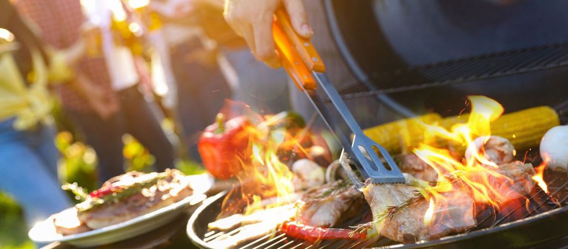 Food cooking on a grill with people socialising in background