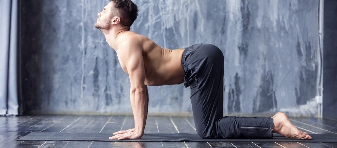 Man performing Cat Cow pose on exercise mat in studio