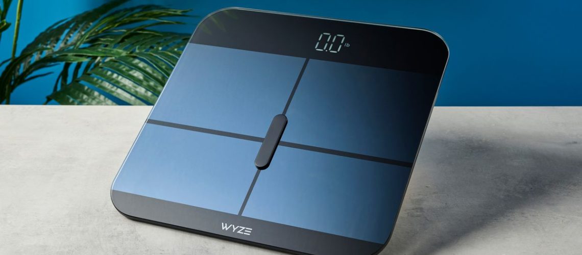 a close up picture of the wyze logo on a sleek, clean-looking smart scale with tempered glass finish and a cross-shaped design on top of the glass, almost blue in the studio lighting, rests upon a table