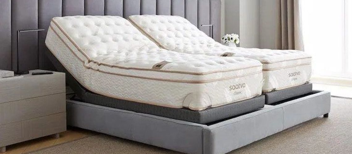 Image shows a Saatva Classic Split King Mattress on a beige fabric bedframe in a neutral colour bedroom