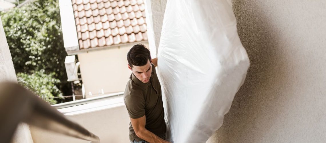A man moves a mattress on his own up a flight of stairs